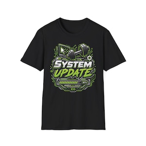 Può includere: Una t-shirt nera a maniche corte con una stampa grafica che riporta il testo SYSTEM UPDATE in bianco e verde. Il design include un manubrio, un monitor di computer con un cursore e una barra di caricamento all'87% con il testo MUSCLE.exe loading.