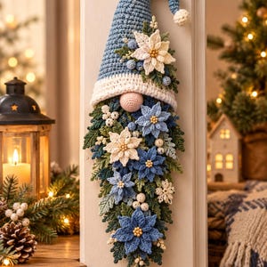 May include: A hanging crochet gnome decoration featuring a tall blue pointed hat with a white brim, a round pink nose, and a long beard composed of layered green leaves, white berries, and various blue and white crocheted poinsettia flowers.