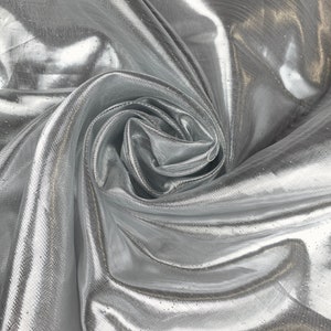 May include: Silver metallic fabric with a shimmering, iridescent finish. The fabric is draped and folded, showcasing its texture and drape.