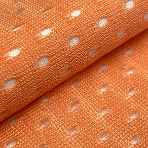 Puede incluir: Primer plano de una tela de color melocot&oacute;n con un patr&oacute;n de lunares blancos. La tela tiene una textura de malla.