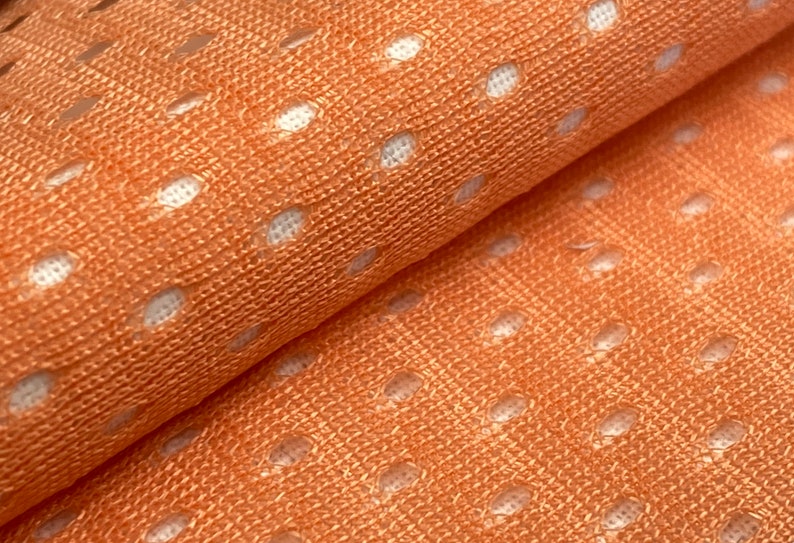 Puede incluir: Primer plano de una tela de color melocot&oacute;n con un patr&oacute;n de lunares blancos. La tela tiene una textura de malla.