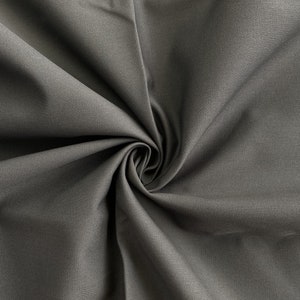 May include: Close-up of a dark gray fabric with a smooth texture. The fabric is folded and draped, creating a soft, flowing look.