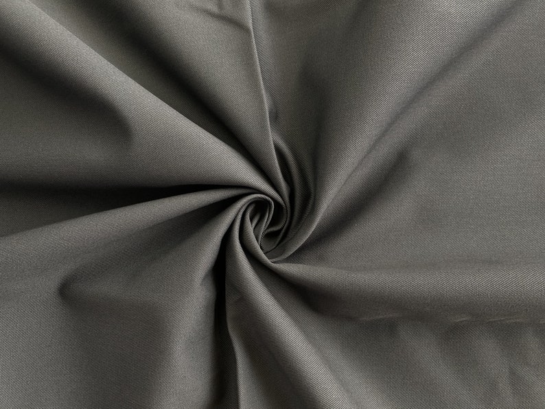 May include: Close-up of a dark gray fabric with a smooth texture. The fabric is folded and draped, creating a soft, flowing look.
