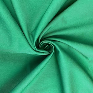 May include: A close-up of a smooth, green fabric with a slight sheen. The fabric is folded and twisted, creating a swirling pattern.