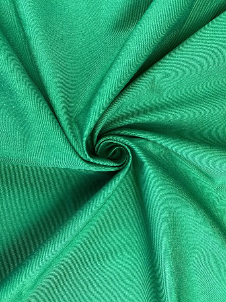 May include: A close-up of a smooth, green fabric with a slight sheen. The fabric is folded and twisted, creating a swirling pattern.