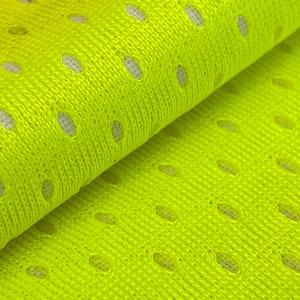 Puede incluir: Primer plano de una tela de malla de color amarillo brillante con peque&ntilde;os agujeros espaciados uniformemente. La tela est&aacute; doblada por la mitad, mostrando la textura y el tejido.