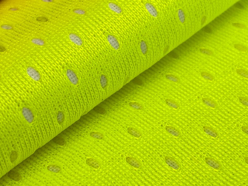 Puede incluir: Primer plano de una tela de malla de color amarillo brillante con peque&ntilde;os agujeros espaciados uniformemente. La tela est&aacute; doblada por la mitad, mostrando la textura y el tejido.