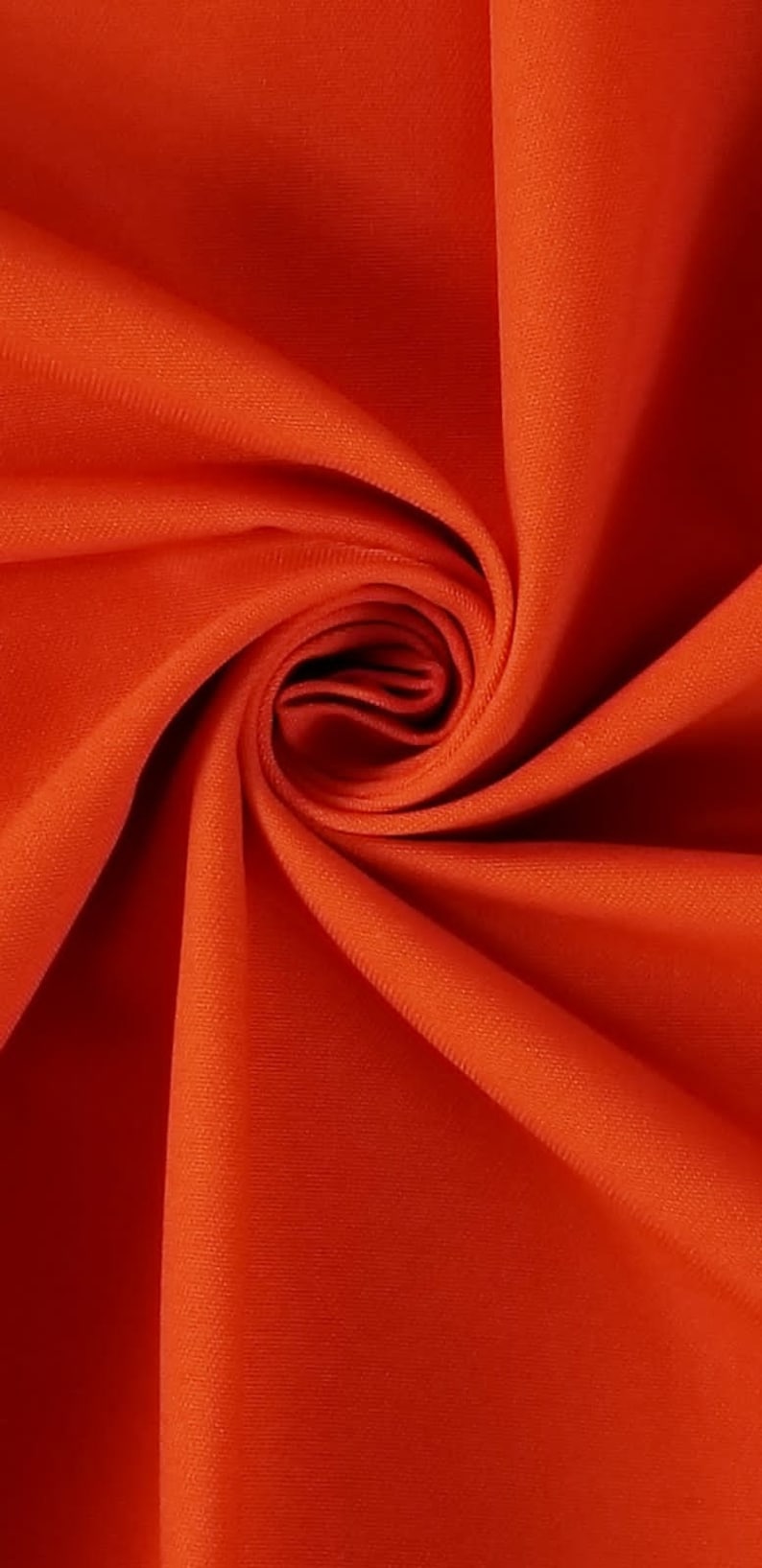 May include: Close-up of a bright orange fabric with a smooth texture. The fabric is folded and draped, creating a soft, flowing look.
