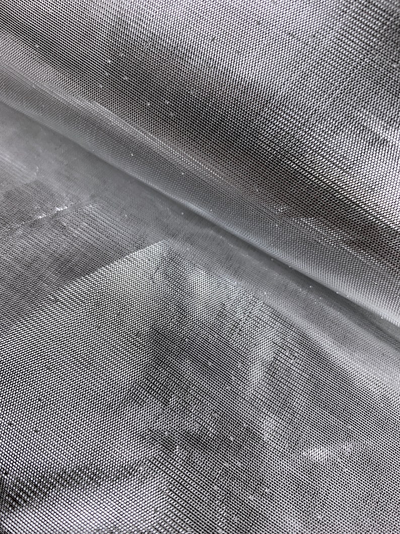 May include: Close-up of a silver-colored mesh fabric with a fine, even weave. The fabric is folded in half, creating a diagonal line across the image.