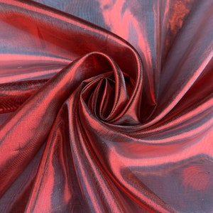 May include: A close-up of a red iridescent fabric with a silky sheen. The fabric is draped and folded, creating a soft, flowing texture.