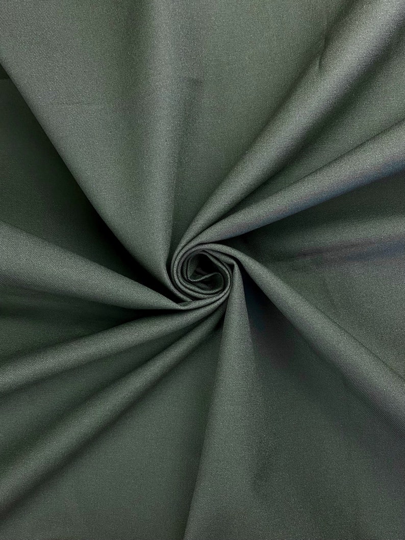 May include: Close-up of a dark green fabric with a smooth texture. The fabric is folded and draped, creating a soft, flowing look.