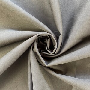 May include: Close-up of a dark gray fabric with a smooth, slightly textured surface. The fabric is folded and twisted, creating a swirling pattern.