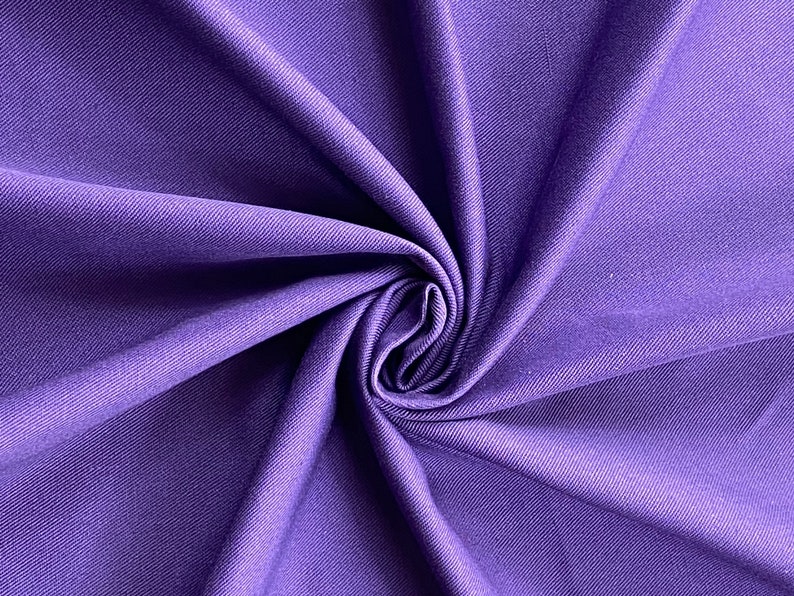 May include: Purple stretch fabric with a smooth, slightly textured surface. The fabric is folded and twisted, showing its drape and flexibility.