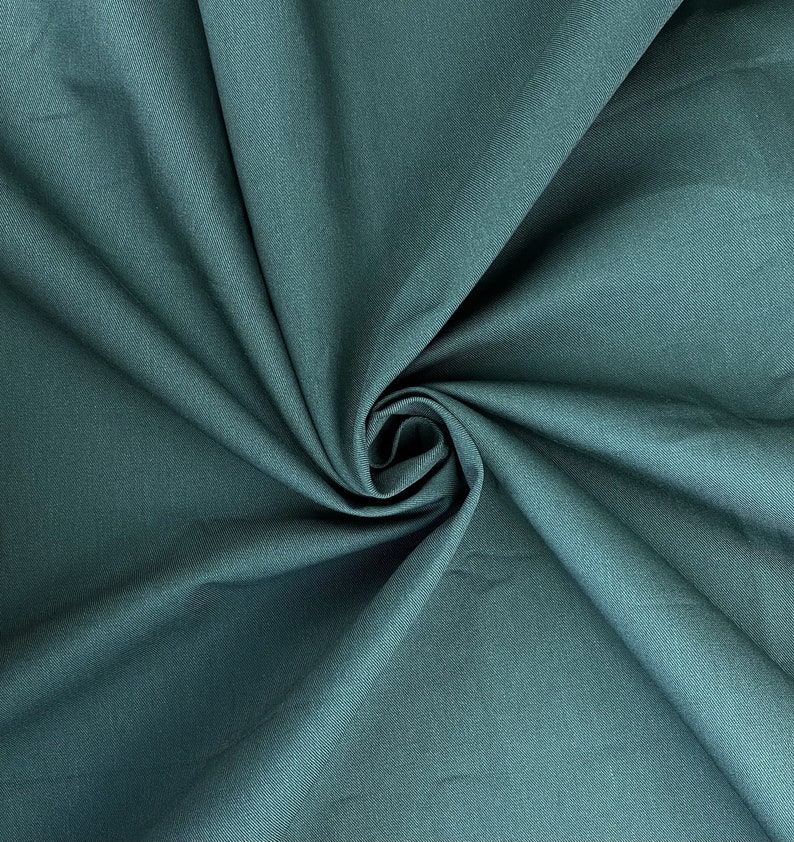 May include: A close-up of a teal fabric with a smooth texture. The fabric is folded and draped, creating a soft, flowing look.