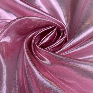 May include: Pink iridescent sheer fabric with a soft, flowing texture. The fabric is folded and draped, showcasing its shimmery and translucent qualities.
