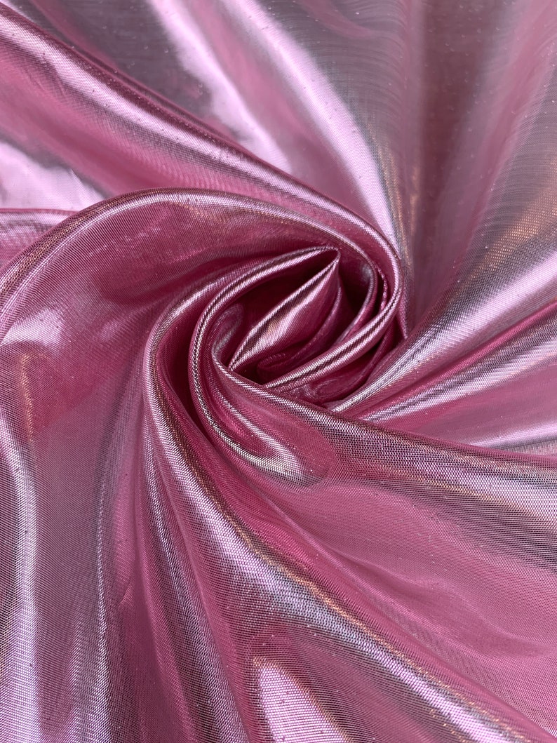 May include: Pink iridescent sheer fabric with a soft, flowing texture. The fabric is folded and draped, showcasing its shimmery and translucent qualities.