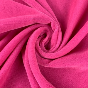 May include: Close-up of a soft, pink velvet fabric. The fabric is folded and draped, showing its texture and color.