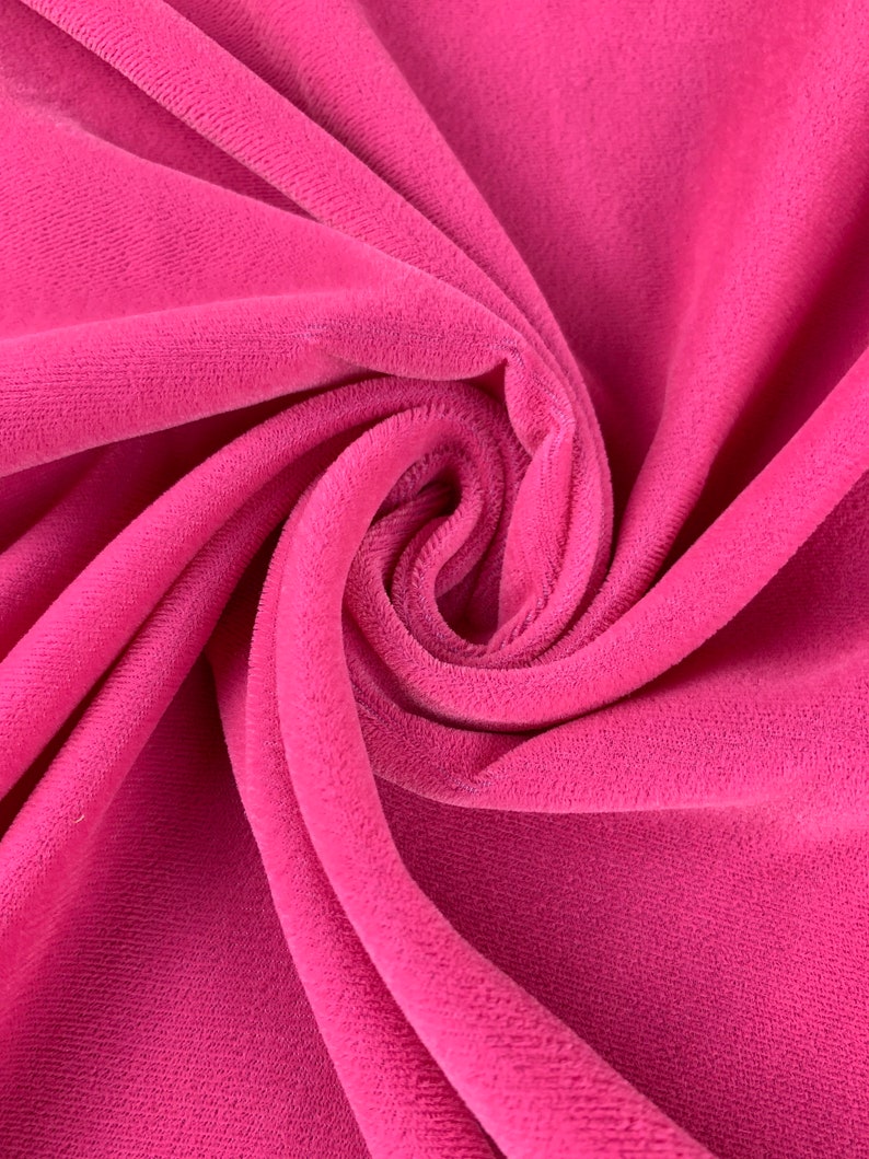 May include: Close-up of a soft, pink velvet fabric. The fabric is folded and draped, showing its texture and color.
