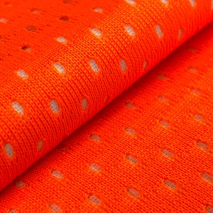 Puede incluir: Tela de malla naranja con un patr&oacute;n repetitivo de peque&ntilde;os agujeros. La tela est&aacute; doblada por la mitad, mostrando la textura y el tejido.