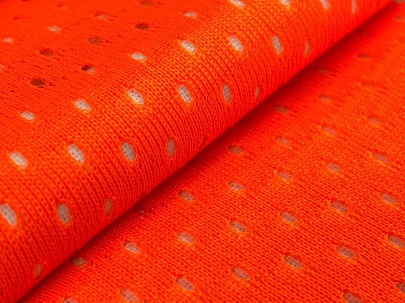 Puede incluir: Tela de malla naranja con un patr&oacute;n repetitivo de peque&ntilde;os agujeros. La tela est&aacute; doblada por la mitad, mostrando la textura y el tejido.