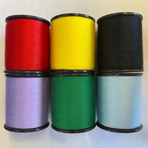 Könnte beinhalten: Sechs Garnrollen in verschiedenen Farben: Rot, Gelb, Schwarz, Lavendel, Grün und Hellblau. Die Rollen sind alle gleich groß und haben schwarze Plastikkappen.