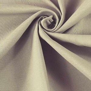 May include: A close-up of a beige fabric with a smooth texture. The fabric is folded and twisted, creating a swirling pattern.