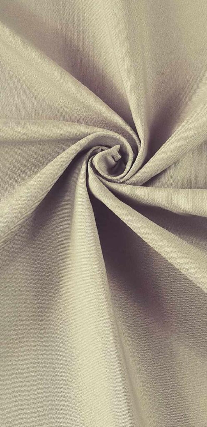 May include: A close-up of a beige fabric with a smooth texture. The fabric is folded and twisted, creating a swirling pattern.