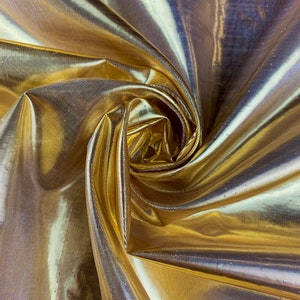 May include: Gold metallic fabric with a shimmery finish. The fabric is draped and folded, creating a soft, flowing texture.
