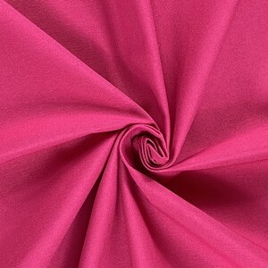 May include: Close-up of a vibrant pink fabric with a smooth, slightly textured surface. The fabric is folded and twisted, creating a dynamic and abstract pattern.