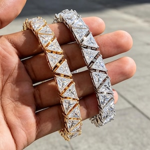 Puede incluir: Dos pulseras de tenis con una serie de piedras transparentes de corte triangular engastadas en marcos de metal. Una pulsera tiene un acabado en tono dorado cálido, mientras que la otra tiene un acabado en tono plateado, con diseño geométrico.