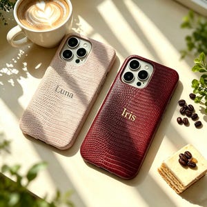 Peut inclure: Deux coques de smartphone avec un motif texturé en peau de lézard. L'une est beige clair avec le nom Luna embossé au centre, et l'autre est bordeaux foncé avec le nom Iris embossé en lettres dorées au centre.
