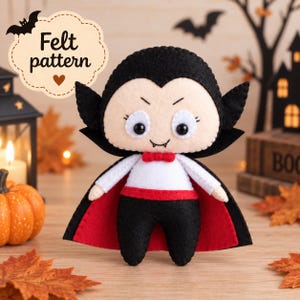 May include: A handcrafted felt vampire doll featuring a black cape with a red lining, a white shirt, black trousers, and a small red bowtie. The doll has a pale face, black hair, and two small fangs. A label above reads Felt pattern.