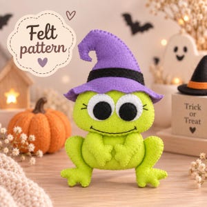 May include: A lime green felt frog plushie wearing a purple witch hat with a black band. The frog has large white eyes with black pupils and stitched eyelashes. A text bubble in the upper left corner reads Felt pattern with a heart icon.