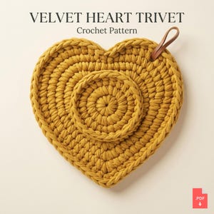 May include: A mustard yellow heart-shaped crochet trivet with a circular center detail and a small brown leather loop attached to the top right edge. The text VELVET HEART TRIVET Crochet Pattern is displayed above the item in a dark font.