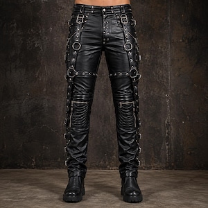 May include: Black pants featuring a faux leather finish, multiple silver-toned metal buckles, straps, and circular rings along the legs. The design includes zippered pockets on the thighs, reinforced knee sections, and a button fly closure.