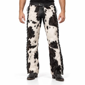 May include: Cowhide leather chaps featuring a black and white spotted pattern. The chaps include a black leather waistband with a central button closure and black leather lacing running down the outer seams of each leg, paired with black boots.
