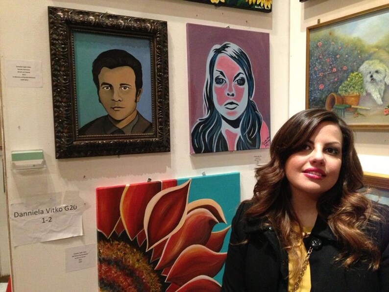 May include: A gallery wall display featuring three paintings: a portrait of a man in a dark ornate frame, a stylized portrait of a person with pink skin tones, and a large close-up painting of a sunflower with red and orange petals on a teal background.