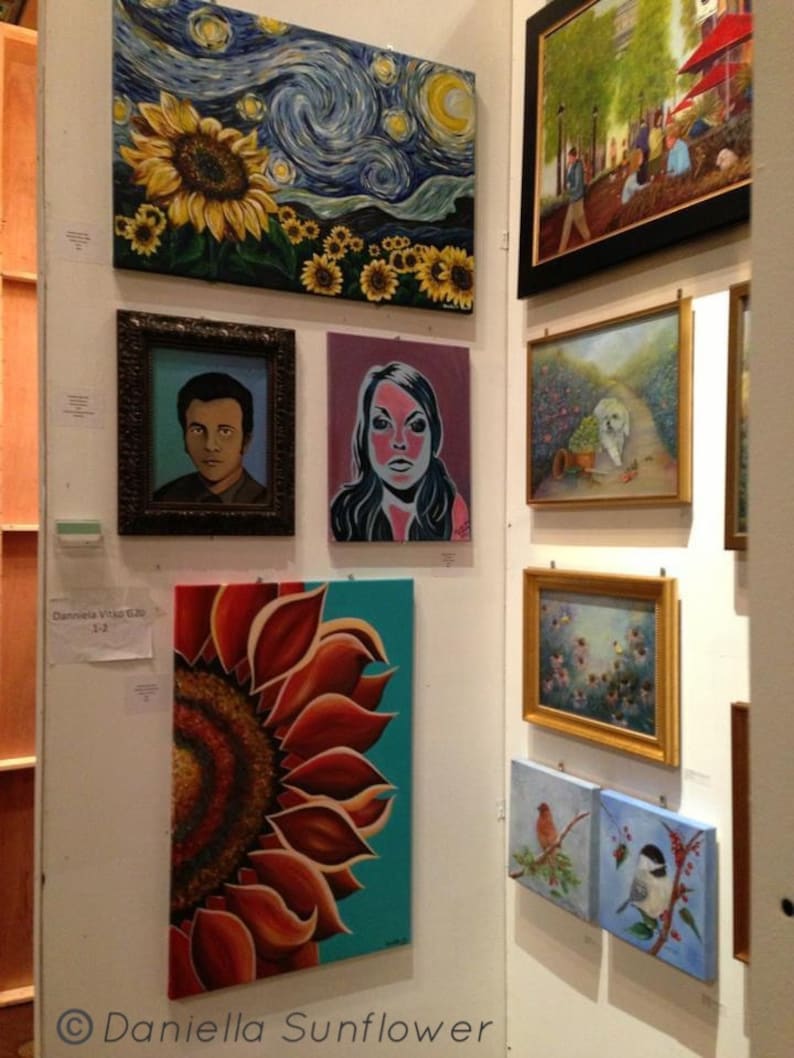 May include: A gallery wall display featuring multiple framed and unframed paintings, including a large sunflower and starry night scene, a portrait of a person, a stylized face, a close-up of a sunflower, a park scene, a dog, and bird paintings.
