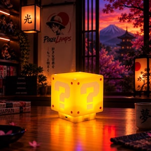 May include: A glowing yellow cube-shaped lamp featuring a white question mark on each visible side, with small red circular accents at the corners. The lamp sits on a wooden surface, emitting a warm light that illuminates the surrounding area.
