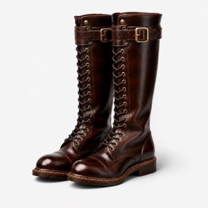 Könnte beinhalten: Ein Paar kniehohe Stiefel aus dunkelbraunem Leder mit Schnürung an der Vorderseite, Metallösen, abgerundeter Zehenkappe und einem dekorativen Riemen am oberen Schaft, der mit einer goldfarbenen Metallschnalle und passenden Beschlägen versehen ist.