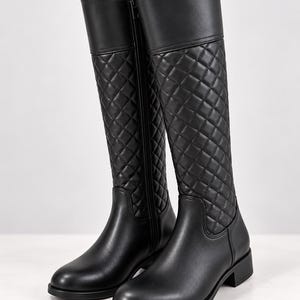 May include: A pair of black knee-high boots featuring a smooth leather-like finish on the rounded toe and heel, with a quilted diamond-patterned shaft. Each boot includes a vertical side zip closure and a low, flat block heel for stability.