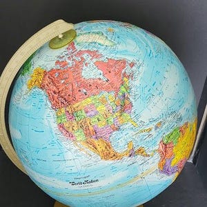May include: A detailed, colorful globe with a light blue ocean and multi-colored continents. The globe is mounted on a gold-colored base and has a beige meridian ring. The text "World Nation" is visible on the globe.