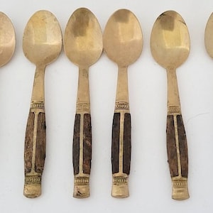 May include: Set of six gold-tone spoons with brown wooden handles. The spoons have a simple, elegant design.
