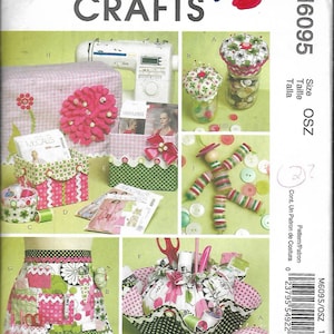 May include: Sewing craft pattern with instructions for making a variety of storage containers and accessories. The pattern includes a pincushion, a sewing needle holder, a button jar, a sewing machine organizer, and an apron. The pattern is printed on a white background with pink and green accents.