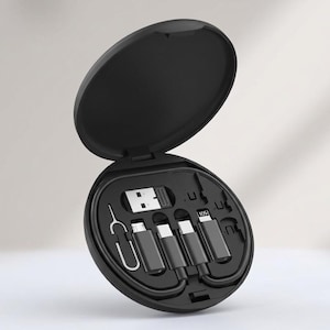 Puede incluir: Un estuche de almacenamiento circular negro que contiene un kit de cable de carga multifuncional. El kit incluye un conector USB-A, una herramienta de expulsión de tarjeta SIM y varios adaptadores, incluidos Micro-USB, USB-C y conectores Lightning etiquetados como iOS.