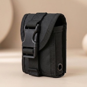 May include: A black rectangular tactical pouch made of durable woven fabric. It features a large plastic side-release buckle closure on the front flap, reinforced stitching, and a small metal grommet hole located on the lower right side panel.