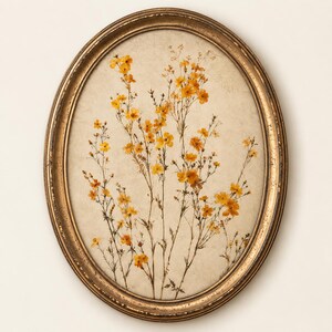 Könnte beinhalten: Ein ovaler Wandrahmen mit abgenutztem Goldfinish, der ein gepresstes botanisches Arrangement enthält. Das Kunstwerk zeigt zarte gelbe Blumen mit dünnen grünen Stielen und Blättern auf einem strukturierten, cremefarbenen Papierhintergrund.