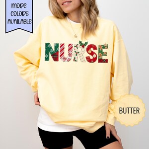 Könnte beinhalten: Ein buttergelbes Langarm-Sweatshirt mit dem Wort NURSE auf der Brust in großen Blockbuchstaben. Jeder Buchstabe zeigt ein anderes festliches Weihnachtsmuster, darunter rot-grünes Karomuster, Pfefferminz-Wirbel, Stechpalmenblätter und Lebkuchenmänner.