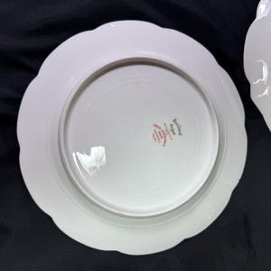 May include: Two white porcelain plates with scalloped edges. The underside of one plate shows the text "Haviland France" in red lettering. The plates are on a dark surface.