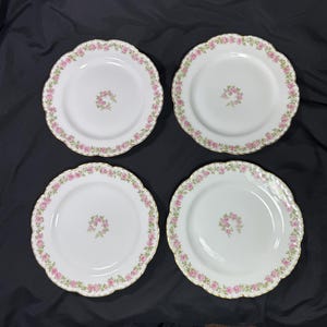 May include: Four white plates with scalloped edges, each adorned with a delicate pink floral border and a central floral cluster. The plates have a gold trim.